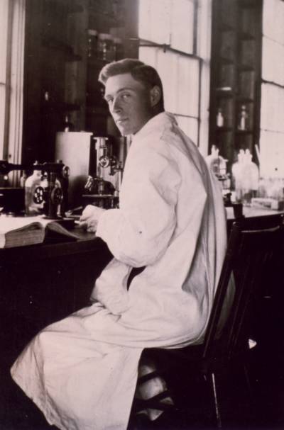 James Collip istuu laboratoriossa työpöydän ääressä päällään valkoinen tutkijan takki.
