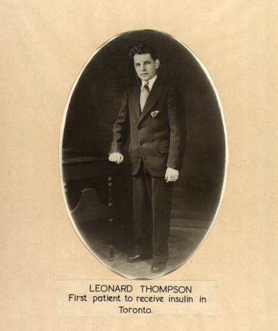 Leonard Thompson nojaa kädellään kirjoituspöytään päällään miesten puku.