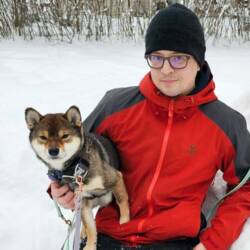 Niila Jouppila istuu talvisessa maisemassa kainalossaan shiba-rotuinen koira.